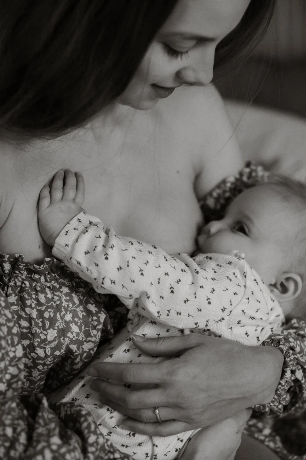 černobílá fotka zblízka zachycující maminku v něžných šatech při kojení