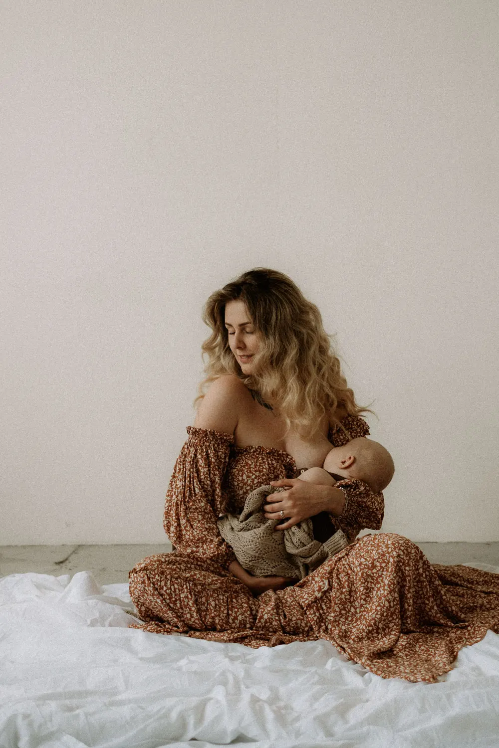 krásná maminka v romantických šatech sedí na zemi a kojí své miminko