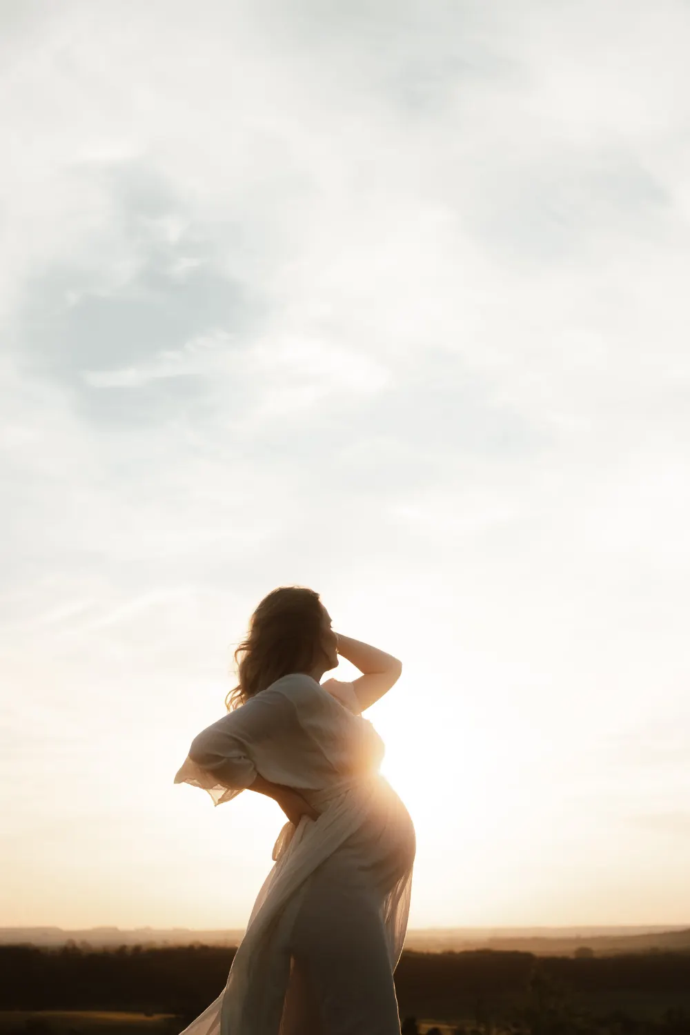 těhotenské fotografie v přírodě - žena stojí na vrcholu kopce při západu slunce v rozevlátých šatech