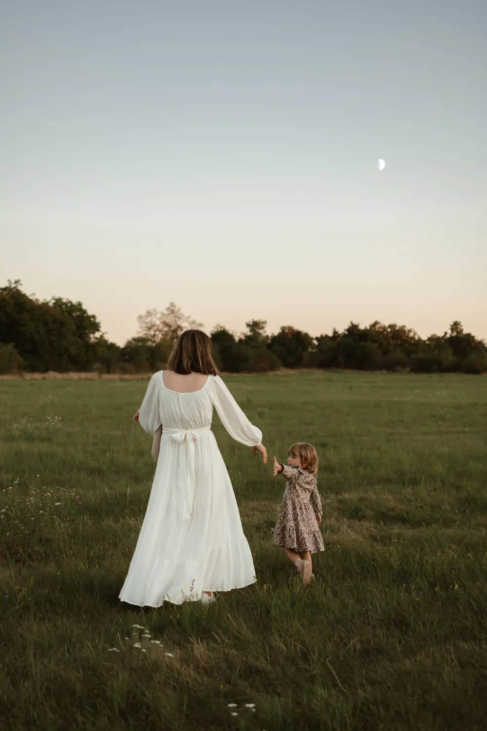 maminka v bílých šatech kráčí po louce s malou dcerou