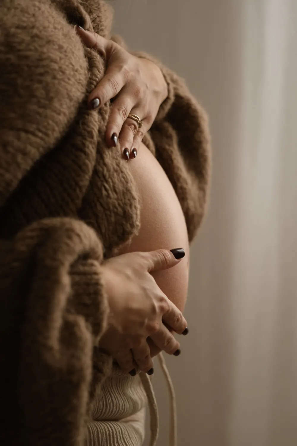 detailní záběr na ruce držící těhotenské bříško. Žena je oblečena v oversized svetru